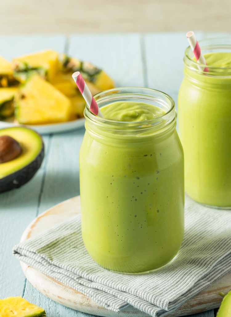 green smoothie in a glass jar with avocado and pineapple in the background